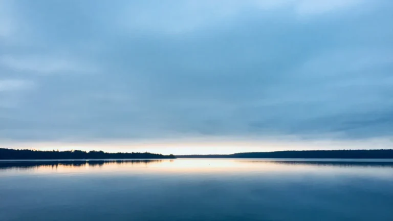 A wide, calm lake at dusk as the sun sets
